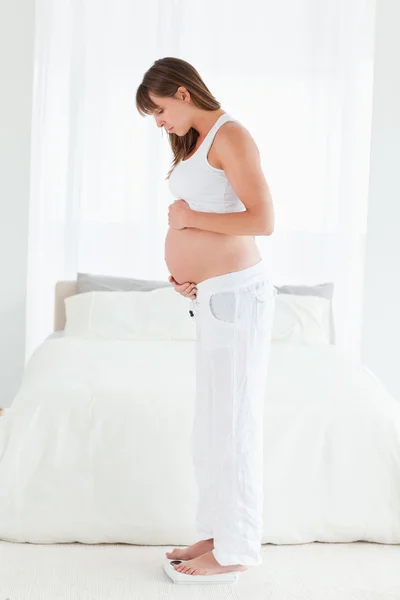 Atractiva hembra embarazada usando una escala mientras está de pie —  Fotos de Stock