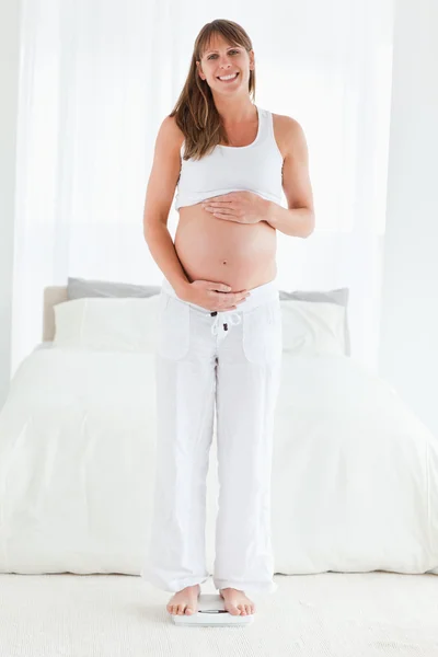 Mulher grávida bonita usando uma escala enquanto em pé — Fotografia de Stock