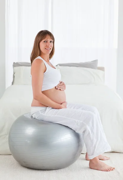 Привлекательная беременная женщина ласкает живот, сидя — стоковое фото