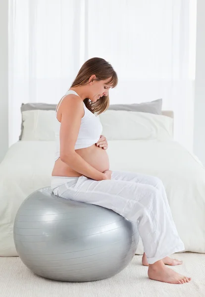 Хорошо выглядящая беременная женщина ласкает живот, сидя — стоковое фото