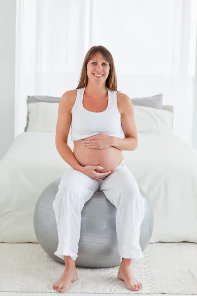 Ziemlich schwangere Frau streichelt ihren Bauch, während sie auf einem gy sitzt — Stockfoto