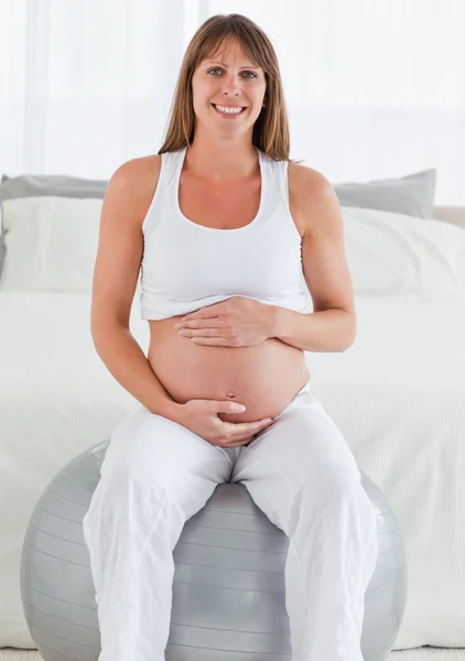 Charmante femme enceinte caressant son ventre tout en étant assis sur un — Photo