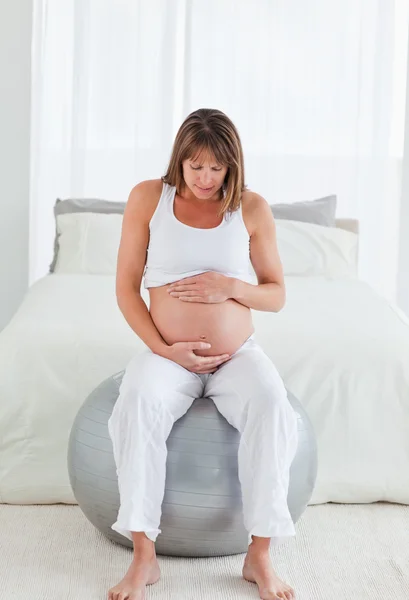 Piękne kobieta w ciąży pieszcząc jej brzuch siedząc na gy — Zdjęcie stockowe