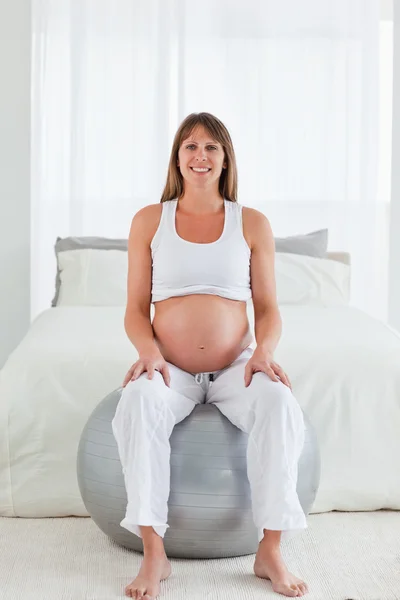 Mulher grávida bonito posando enquanto sentado em uma bola de ginástica — Fotografia de Stock