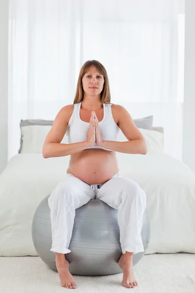 Encantadora mujer embarazada haciendo ejercicios de relajación mientras se sienta — Foto de Stock