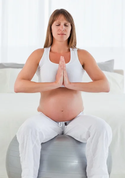 Preciosa mujer embarazada haciendo ejercicios de relajación mientras está sentada —  Fotos de Stock