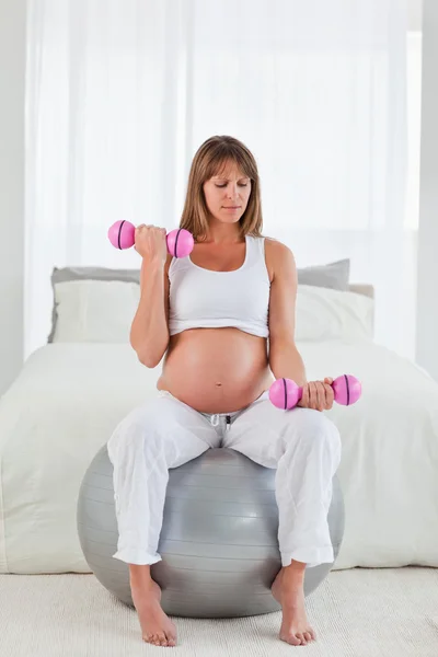 Bela fêmea grávida usando um haltere enquanto sentado em um gy — Fotografia de Stock