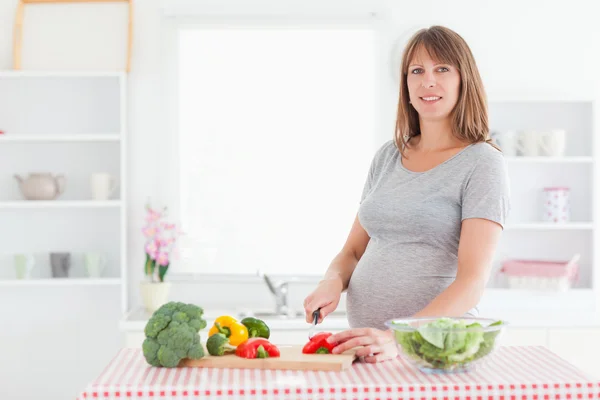 Krásná těhotná žena pózuje při vaření zeleniny — Stock fotografie