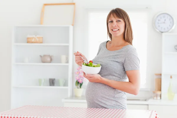 Mujer embarazada encantadora comiendo un tomate cherry mientras está de pie —  Fotos de Stock