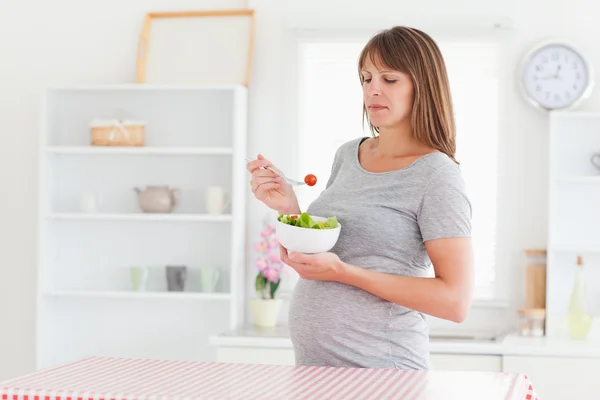 Beautiful pregnant woman eating a cherry tomato while standing — Stock Photo, Image
