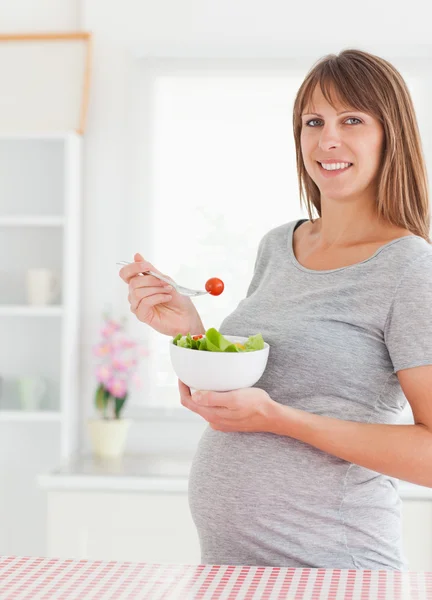 Charmante femme enceinte mangeant une tomate cerise debout — Photo