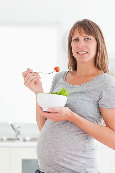 Pretty pregnant woman eating a cherry tomato while standing — Stock Photo, Image