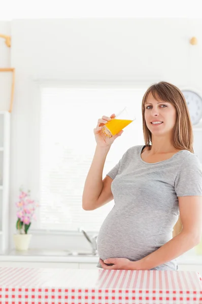 Беременная женщина пьет стакан апельсинового сока, пока она... — стоковое фото