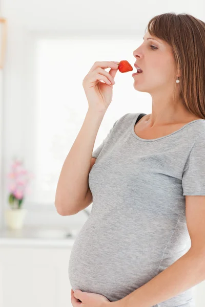 Αρκετά έγκυος γυναίκα τρώει μια φράουλα ενώ στέκεται — Φωτογραφία Αρχείου