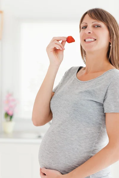 Beautiful pregnant woman eating a strawberry while standing — Stock Photo, Image