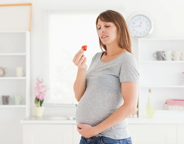 Красивая беременная женщина ест клубнику стоя — стоковое фото