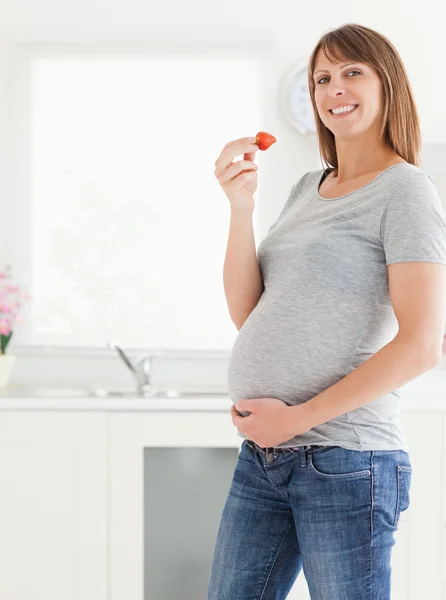 Schöne schwangere Frau isst eine Erdbeere im Stehen — Stockfoto