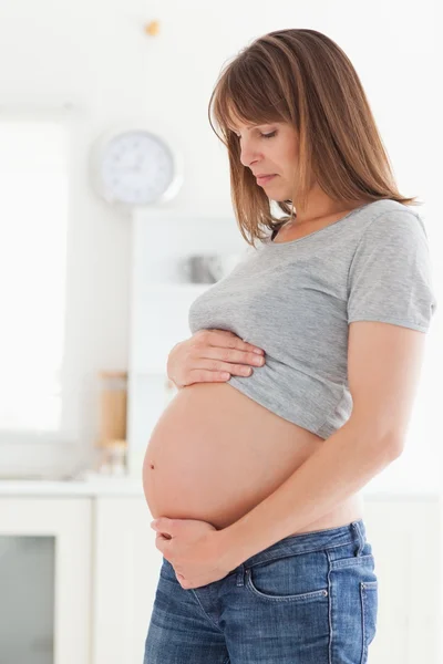Mujer embarazada de buen aspecto posando mientras acaricia su vientre — Foto de Stock