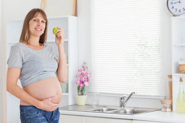 Mulher muito grávida posando enquanto segura uma maçã verde — Fotografia de Stock