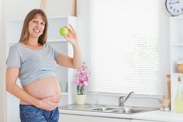 Красивая беременная женщина позирует, держа зеленое яблоко — стоковое фото