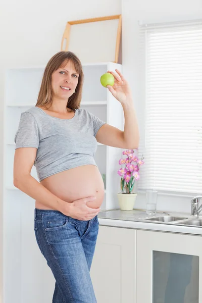 Atractiva mujer embarazada posando mientras sostiene una manzana verde —  Fotos de Stock