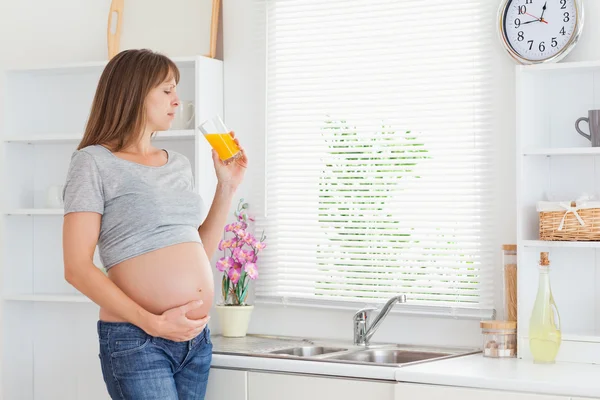 Bella donna incinta che beve un bicchiere di succo d'arancia mentre — Foto Stock