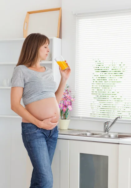 Привлекательная беременная женщина пьет стакан апельсинового сока, пока — стоковое фото