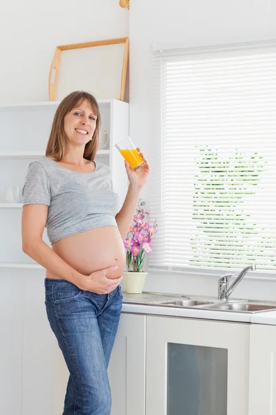 Krásná těhotná žena drží sklenici pomerančového džusu, zatímco s — Stock fotografie