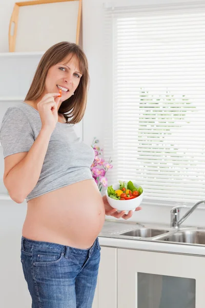 Piękne kobiety w ciąży jedzenia warzyw stojąc — Zdjęcie stockowe