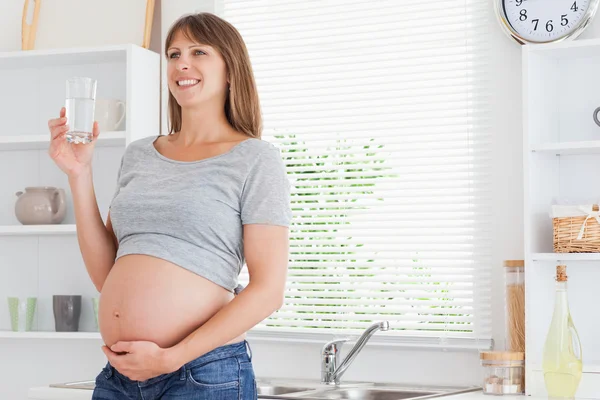 Bardzo ciąży kobieta trzyma kieliszek z wodą stojąc — Zdjęcie stockowe