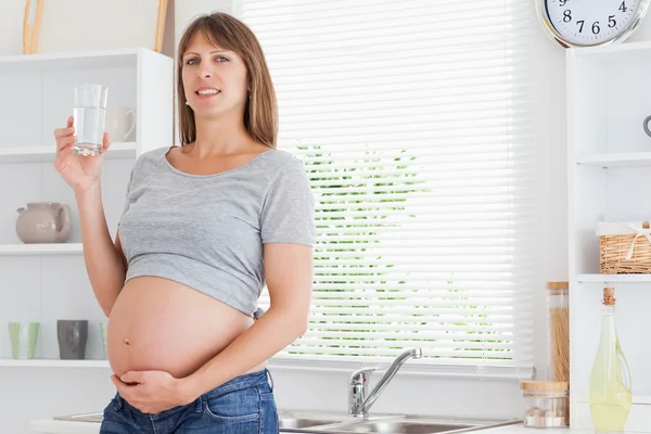 Schöne schwangere Frau mit einem Glas Wasser im Stehen — Stockfoto