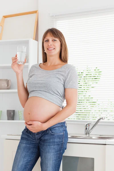 Atrakcyjna kobieta w ciąży trzymając szklankę wody podczas stojącą — Zdjęcie stockowe