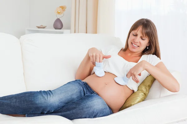 Mooie zwangere vrouw spelen met baby schoenen liggend — Stockfoto
