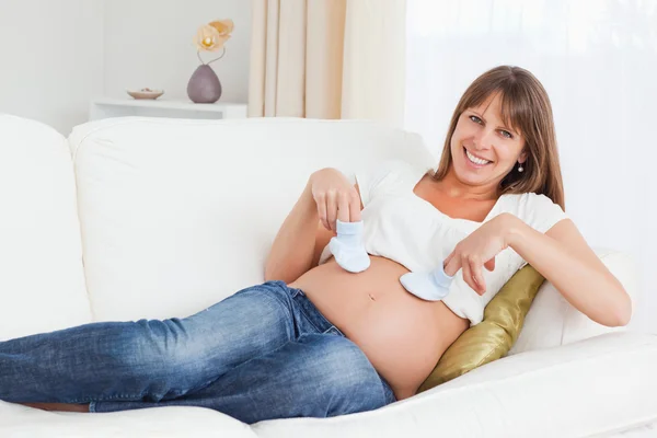 Attraktive Schwangere spielt im Liegen mit Babyschuhen — Stockfoto