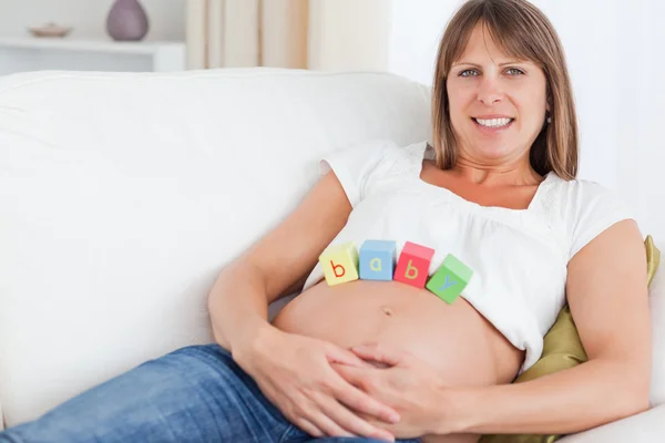 Ziemlich schwangere Frau spielt mit Holzklötzen, während sie auf liegt — Stockfoto