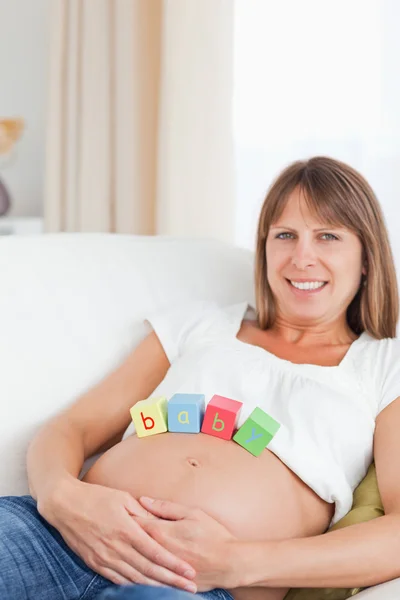 Schöne schwangere Frau spielt mit Holzklötzen, während sie auf liegt — Stockfoto