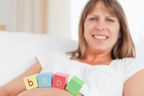 Linda mujer embarazada jugando con bloques de madera mientras está acostada en un —  Fotos de Stock