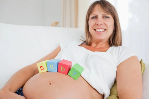 Pretty pregnant female playing with wooden blocks while lying on — Stok fotoğraf