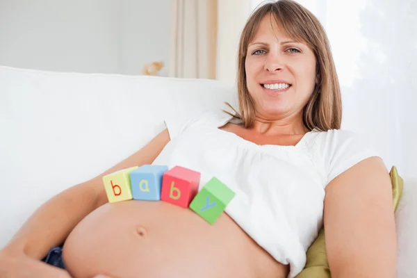 Schöne schwangere Frau spielt mit Holzklötzen, während sie auf liegt — Stockfoto