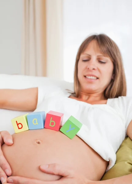 Schöne schwangere Frau spielt im Liegen mit Holzklötzen — Stockfoto