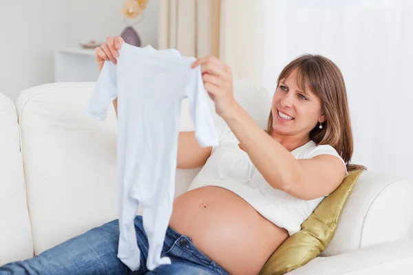 Αρκετά έγκυος γυναίκα που κρατά ένα μωρό αυξάνεται ενώ βρίσκεται σε έναν καναπέ — Φωτογραφία Αρχείου