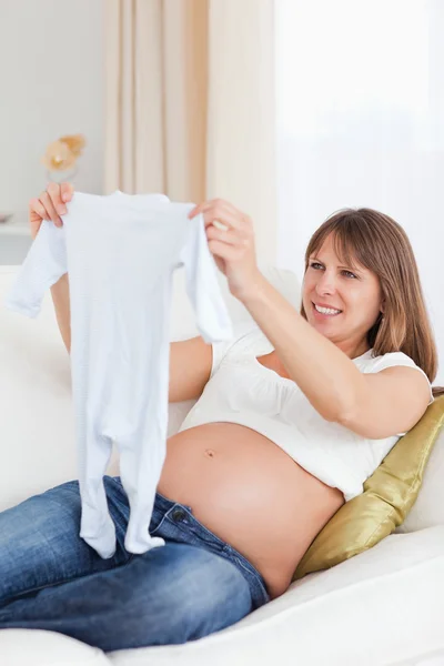 Lovely pregnant woman holding a baby grow while lying on a sofa — Stock Photo, Image