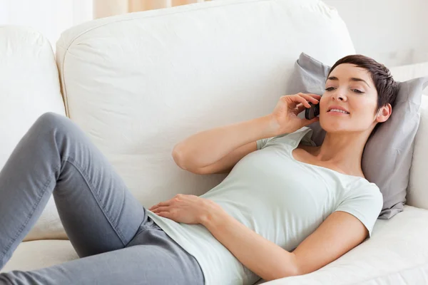 Close up of a brunette calling while lying on a sofa — Stock Photo, Image