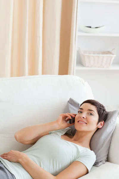 Portrait of a cute brunette calling while lying on a sofa — Stock Photo, Image