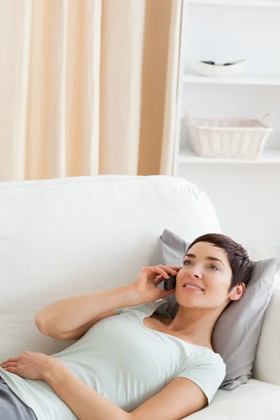 Portrait of a young brunette calling while lying on a sofa — Stock Photo, Image