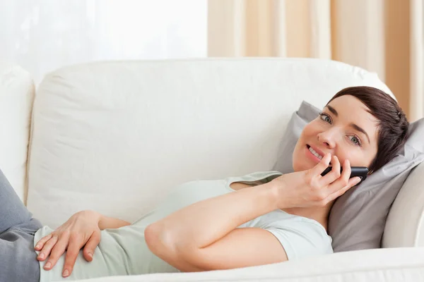 Närbild av en lugn brunett att göra ett telefonsamtal liggande på en — Stockfoto