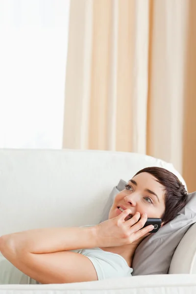 Sonriente morena llamando mientras está acostada en un sofá — Foto de Stock