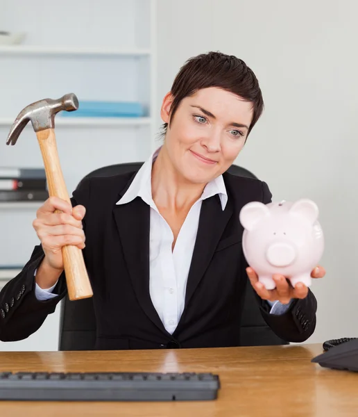 Lachende kantoor werknemer een spaarpot breken met een hamer — Stockfoto