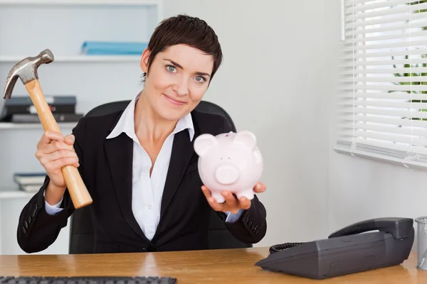 Cute office worker breaking a piggybank with a hammer — Stock Photo, Image