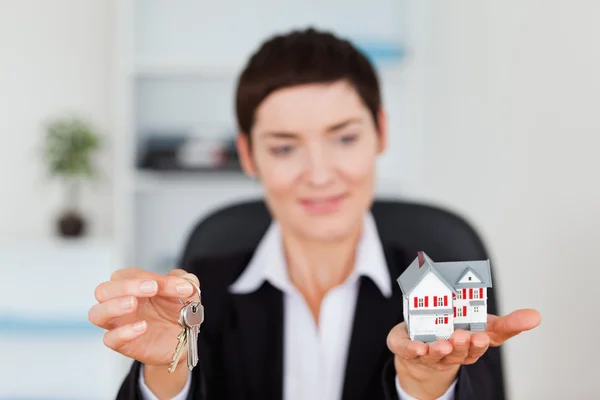 Smiling woman showing a miniature house and a key — Stock Photo, Image